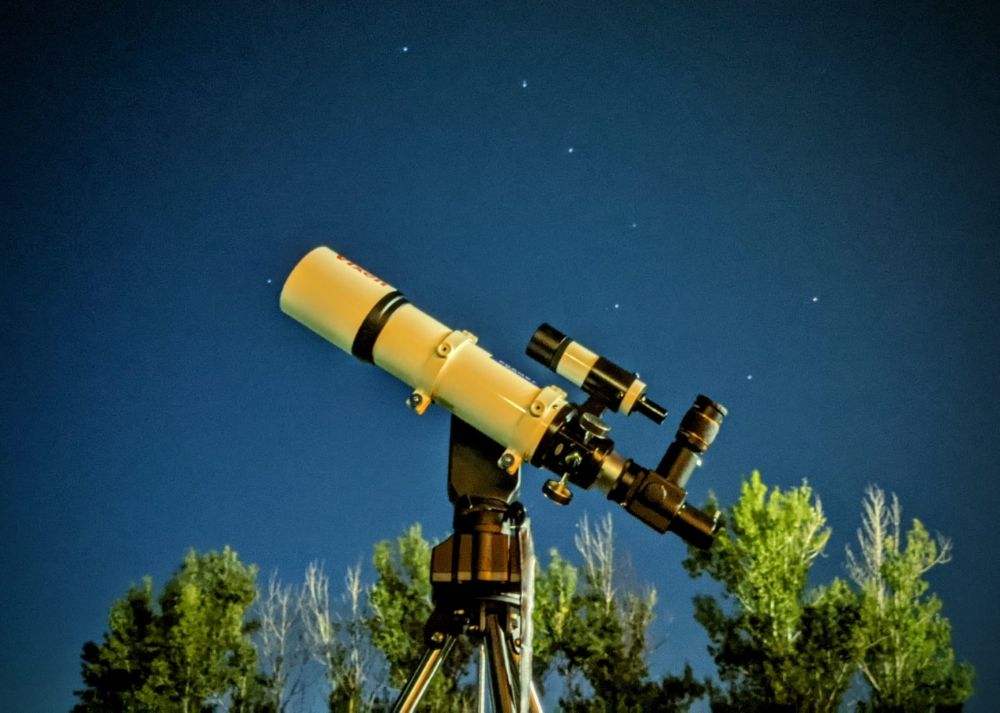 A photo of a telescope with a starry sky behind. The Big Dipper is visible in the night sky.