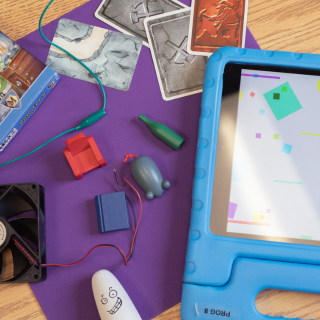 A table with construction paper, a card game, an iPad, and a battery-powered mouse. 