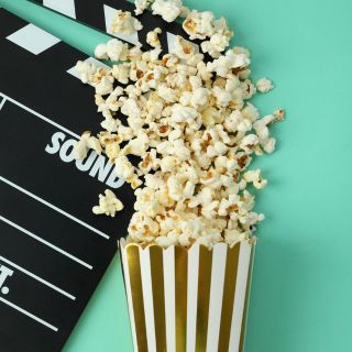 A box of popcorn tipped over and spilling on a movie clack board on a teal background.