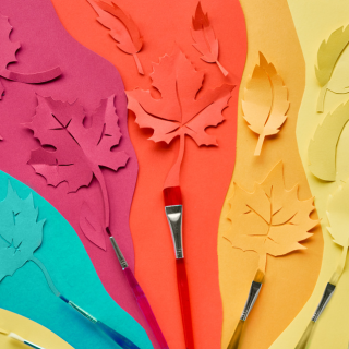 Painted leaves on a multi-coloured background with paint brushes.