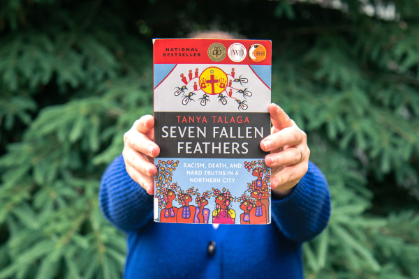 Person holding paperback copy of Seven Fallen Feathers 