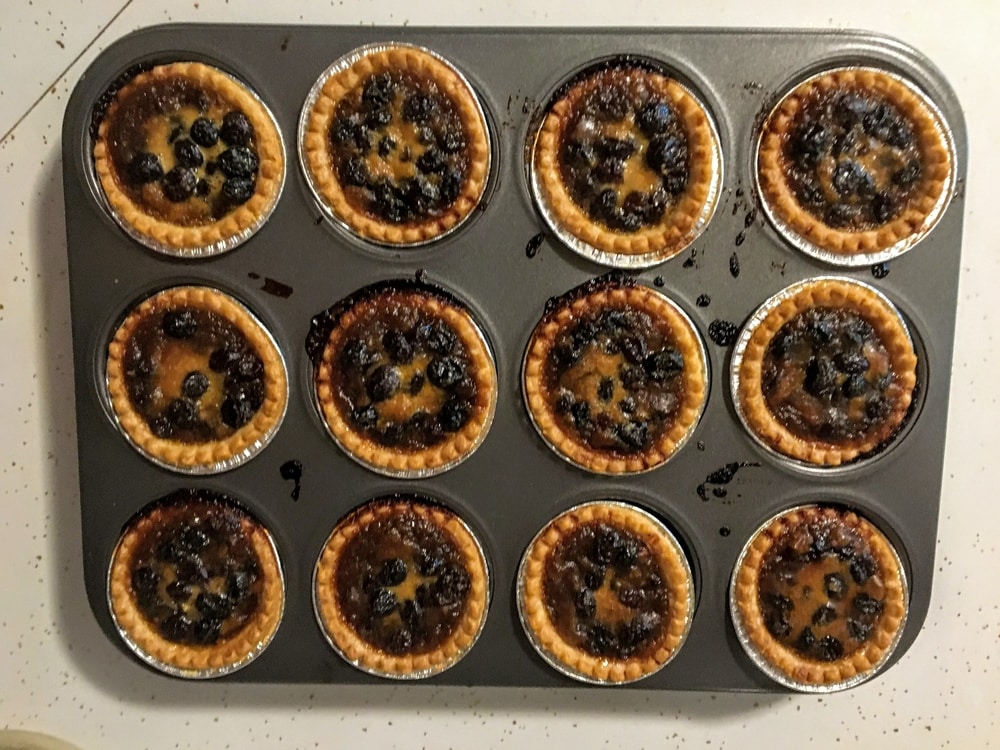 Baked butter tarts with raisins in a muffin tray on a counter.