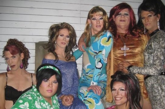A photo of seven gorgeous drag queens posing together in full makeup, hair and outfits.